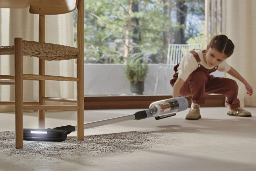 Holčička vysává nepořádek pod židlý s pomocí vysavače Electrolux.
