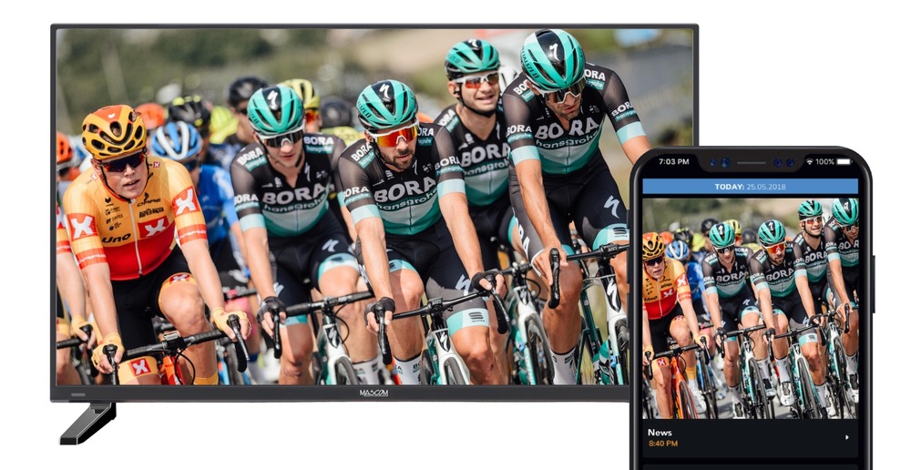 Televize Mascom MC22TFW11 se záběrem cyklistického závodu, před televizí je smartphone, který má na displeji stejný záběr