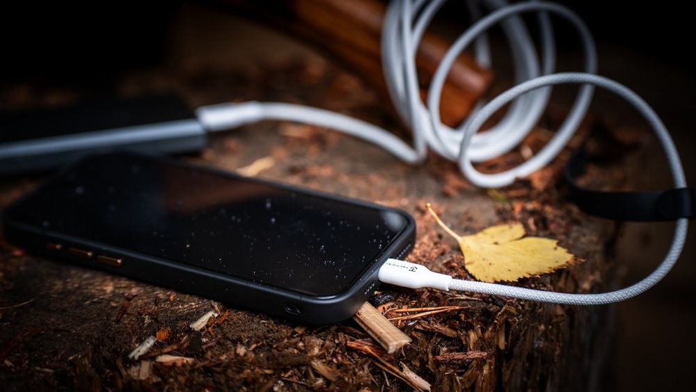 Kabel Tactical Stitch Thread USB-A/Lightning 2m bílý Smartphone položený v přírodě napojený na powerbanku skrz kabel Tactical Stitch Thread