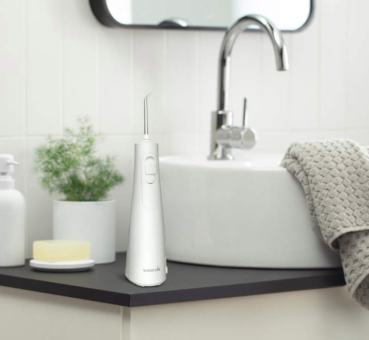 Ústní sprcha Waterpik WF21EU bílá Ústní sprcha Waterpik WF21EU umístěná na koupelnové desce vedle umyvadla a ručníku