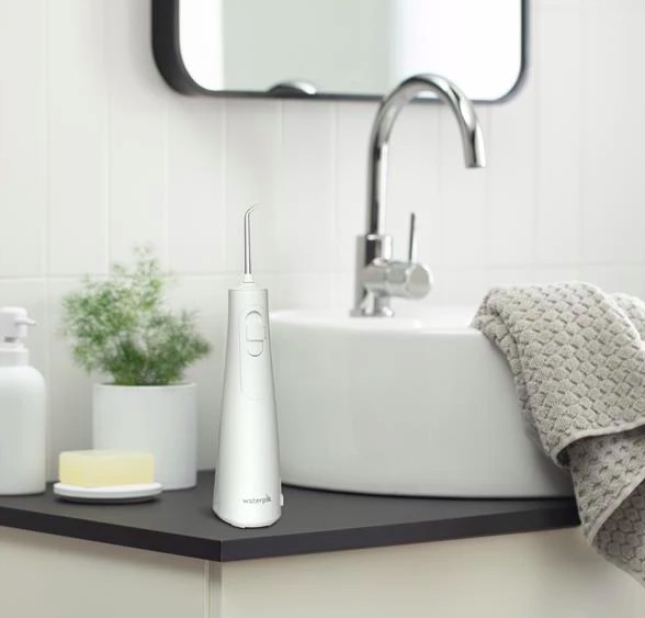 Ústní sprcha Waterpik WF26EU stojí na koupelnové desce vedle umyvadla