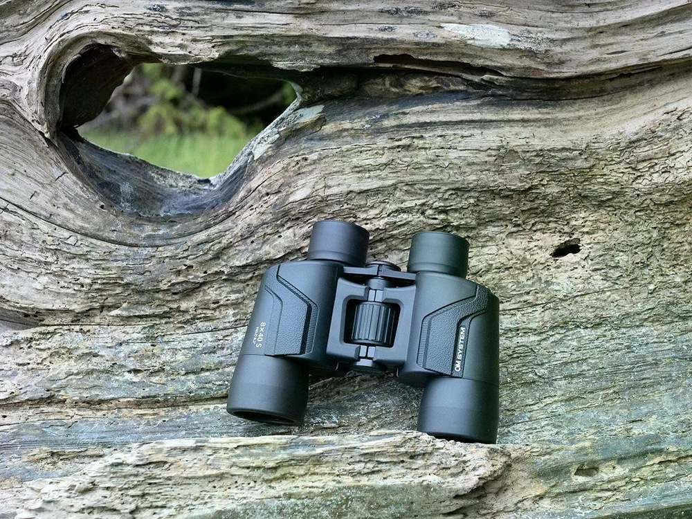 Dalekohled OM SYSTEM 8 x 40 S položený na dřevě v přírodě, detail pogumovaného povrchu