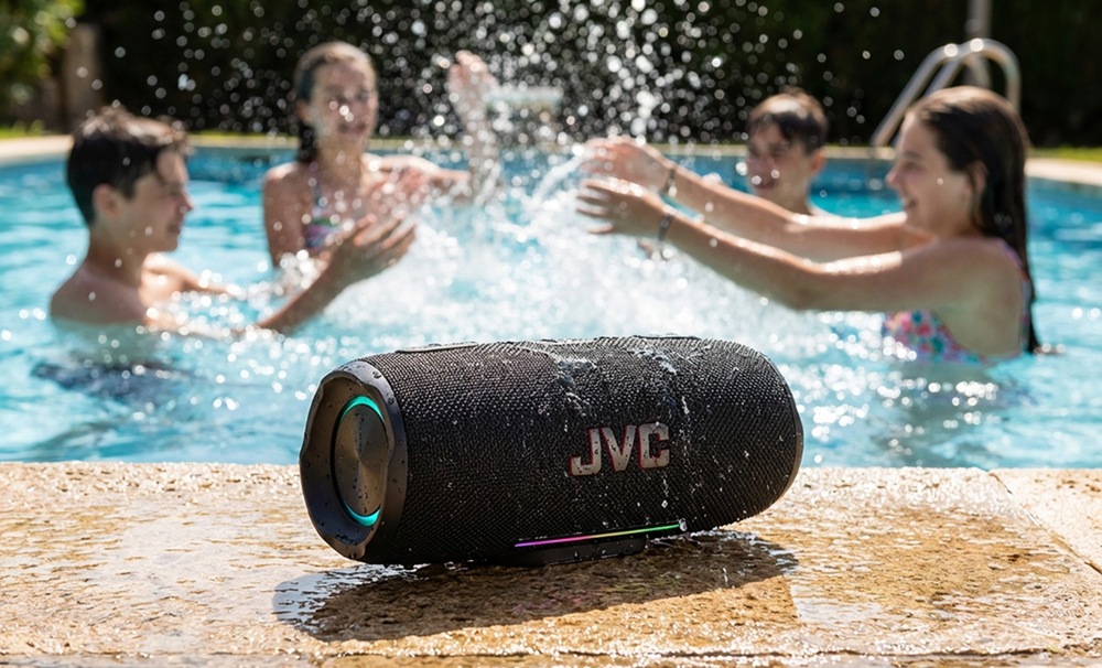 Voděodolný přenosný Bluetooth reproduktor JVC XS-E425B u bazénu se stříkající vodou a dětmi v pozadí