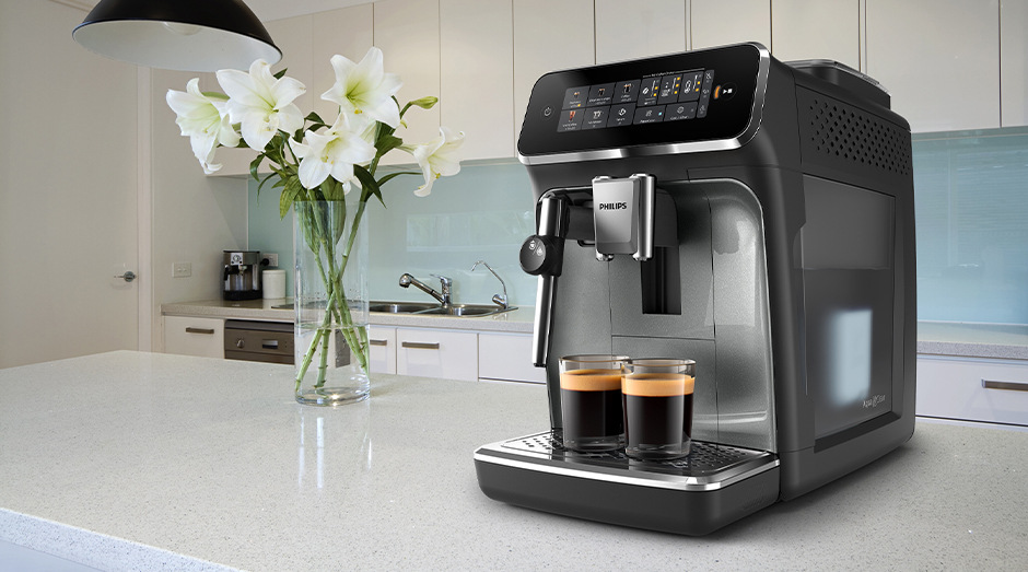 Automatický kávovar Philips EP3329/70 3300 Series stojící na bílé kuchyňské lince vedle vázy s květinami