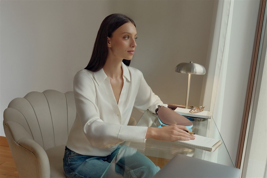 Žena sedí u pracovního stolu a používá masku.
