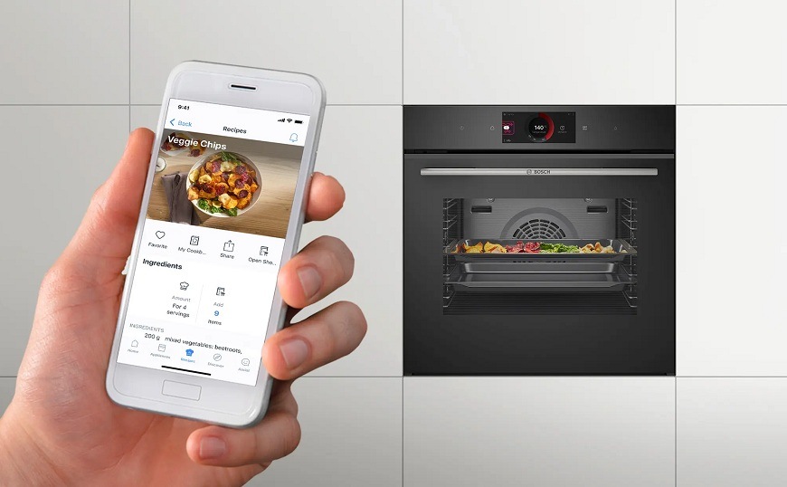 Trouba Bosch Serie 8 HBG774KB1 pyrolýza černá Vestavná trouba Bosch v bílé kuchyňské lince, v přední části ruka s mobilem, na které je aplikace Home Connect