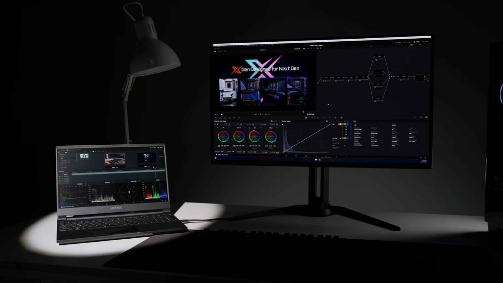 Slabě osvětlený pracovní prostor s notebookem a velkým monitorem s programem pro střih videa. Ilustruje použití funkce KVM.