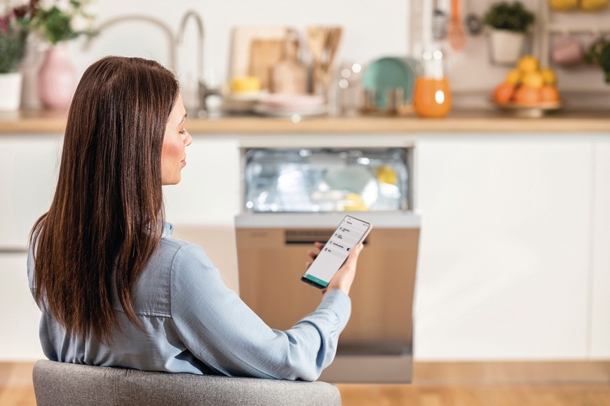 Žena drží v ruce chytré mobilní zařízení, ve kterém má otevřenou mobilní aplikaci ConnectLife. S touto aplikací může myčku Gorenje GORGI673B90X dálkově ovládat i kontrolovat stav či spotřebu vody i elektřiny.
