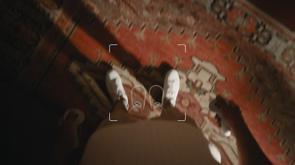 Snímač pohybu PICO Motion Tracker bílé Osoba v bílých botách stojí na červeném vzorovaném koberci a drží v ruce ovladače VR. Viditelné jsou prvky rozhraní virtuální reality, které naznačují pohlcující zážitek.