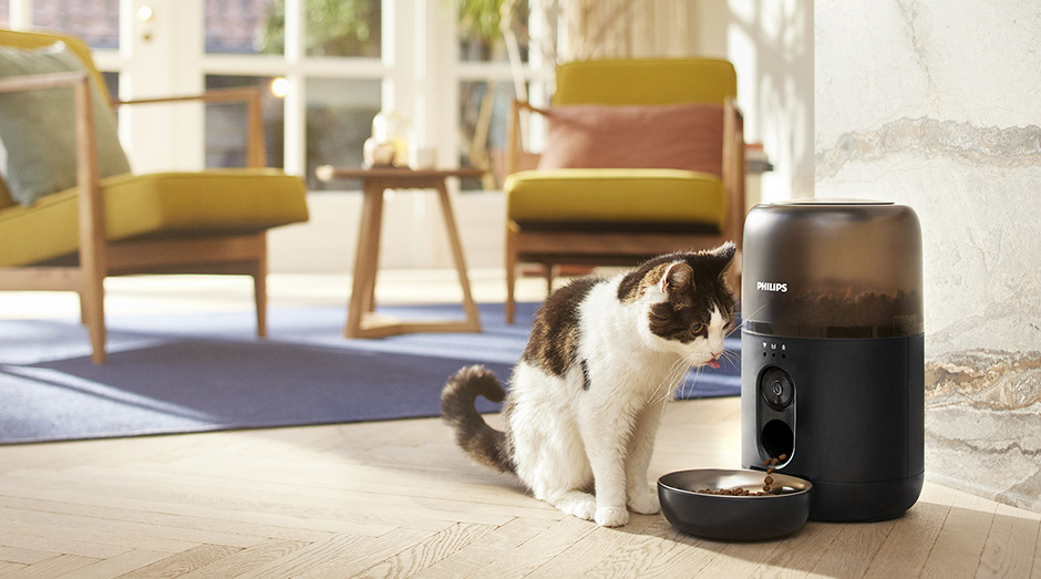 Chytré krmítko Philips a vedle něho sedící kočka, která čeká na krmivo