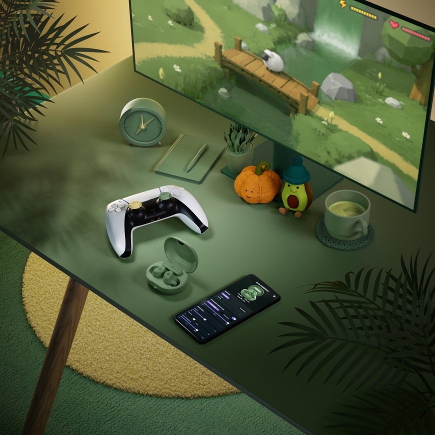 GameBuds Matcha na herním stole s ovladačem PlayStation a mobilní aplikací na telefonu