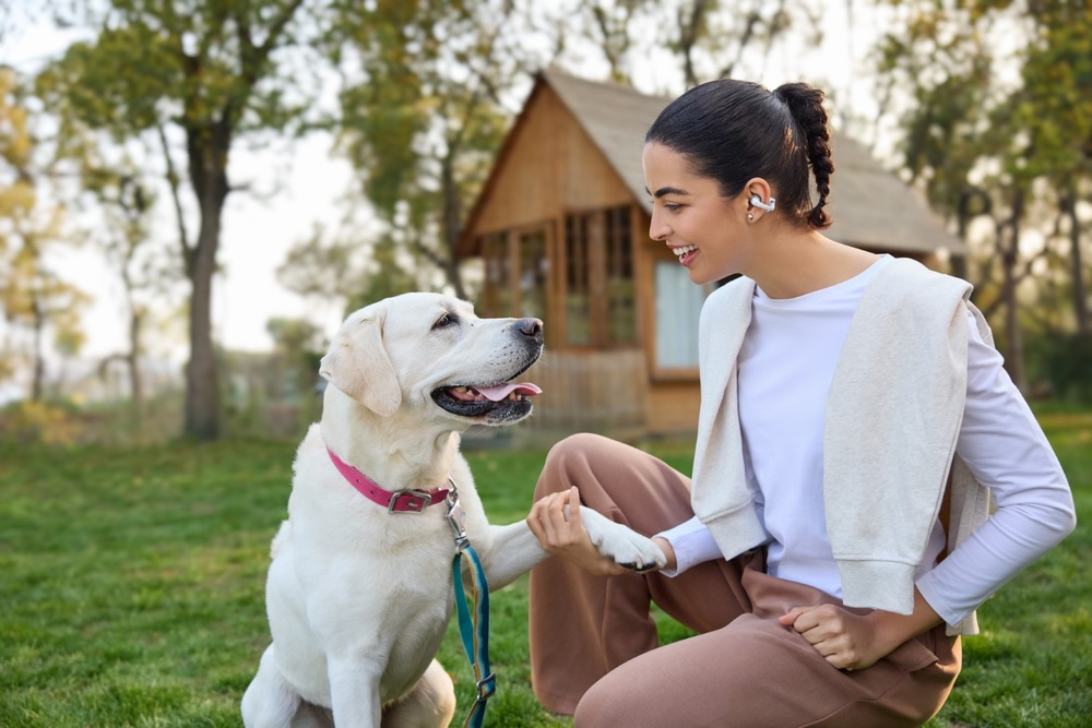 Sluchátka Shokz OpenDots 2, Bluetooth černá Žena sedící se psem na zahradě má na uších klipová sluchátka OpenDots 2