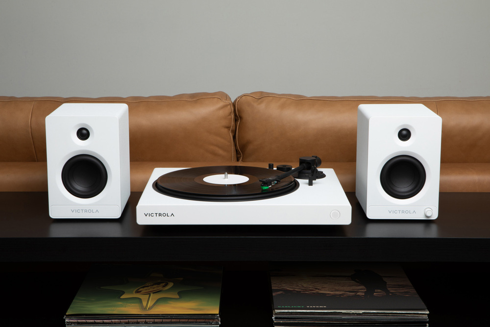 Gramofon Victrola VPT-1520 Wave v bílé barvě zapojený mezi dva regálové reproduktory, domácí poslech vinylů v obývacím pokoji