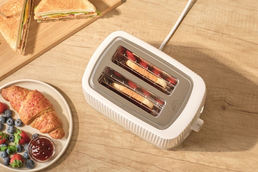 Topinkovač Sencor STS 7510WH bílý Pohled shora na topinkovač Sencor STS 7510WH. Uvnitř se připravují topinky. Vedle na talířku jsou croissanty.