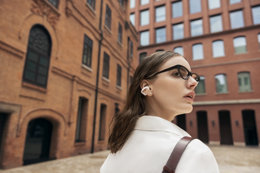 Sluchátka Shokz OpenDots 2, Bluetooth šedá Žena s brýlemi při chůzi po městě používá sluchátka s dlouhou výdrží