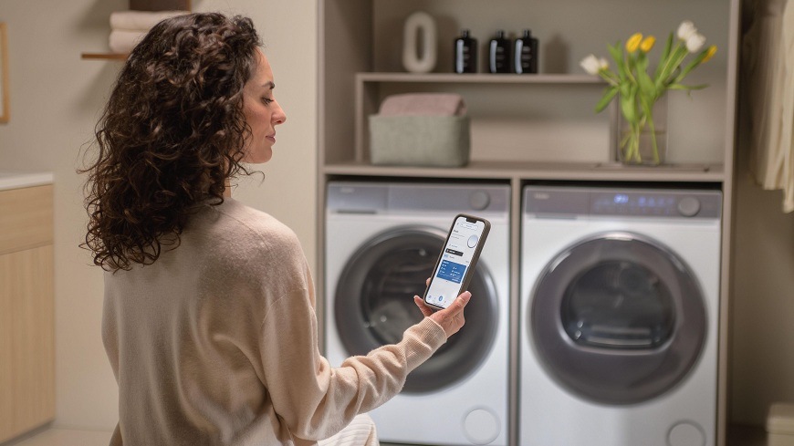 Sušička prádla Haier HD90-A367U1-S bílá žena telefonem ovládá sušičku haier HD90-A367U1-S, která se nachází v prádelně vedle pračky