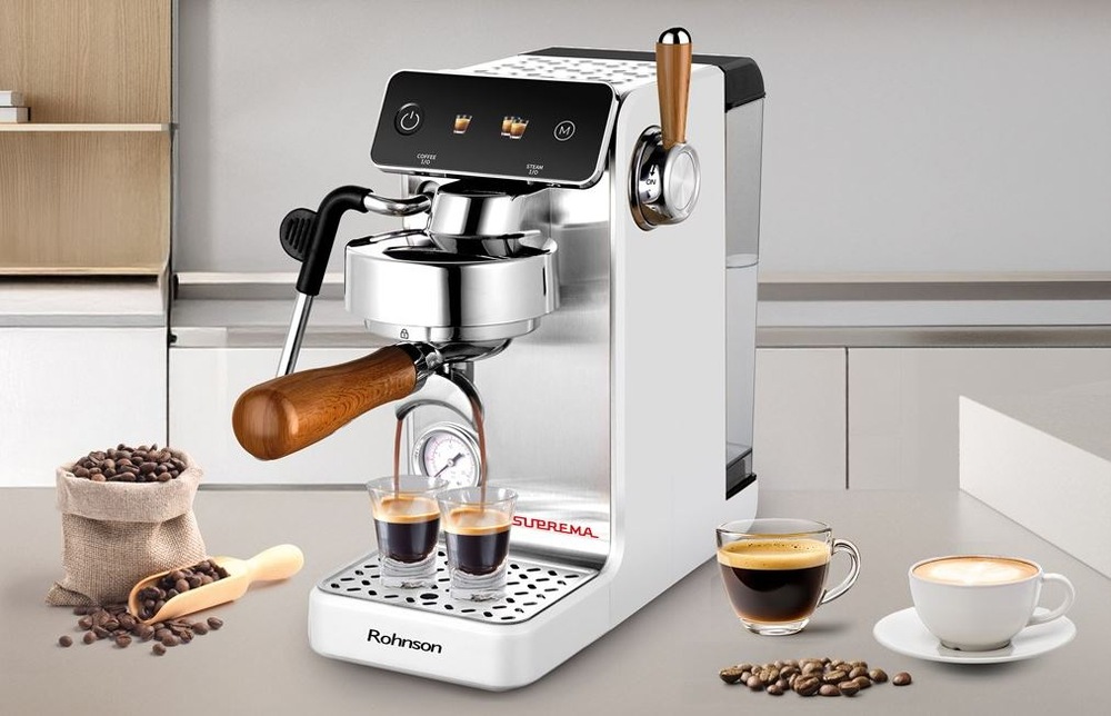 Kávovar Rohnson R-98300 Suprema stojí na kuchyňské lince. Připravuje zároveň dva šálky, vedle něj je pytlík s kávou, na druhé straně stojí espresso a cappuccino.