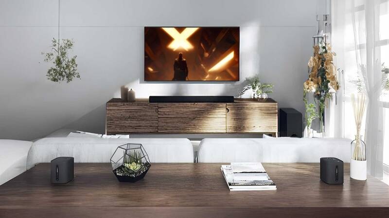 Soundbar Yamaha True X Surround 50A (set) černý soundbar yamaha true x surround 50a umístěný pod televizí v moderním obývacím pokoji s bezdrátovými reproduktory na stole