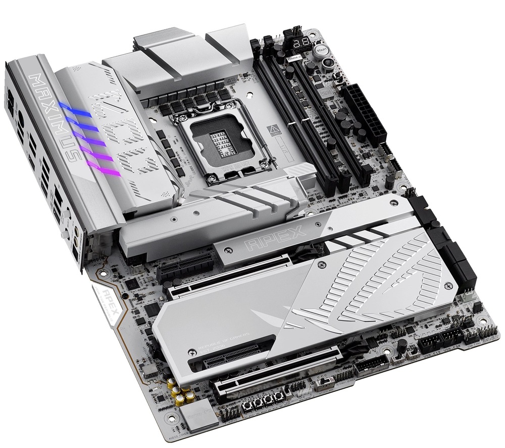 Základní deska Asus ROG MAXIMUS Z890 APEX Na fotce je deska focená shora pod mírným úhlem z pravé strany, takže je vidět hlavně její „povrch“ a vrstevnaté chladiče. Dominuje stříbrno-bílé provedení s velkými pasivy kolem patice procesoru uprostřed a dlouhými kryty pro M.2/čipset ve spodní části. Vpravo nahoře jsou dva DDR5 sloty a u horní hrany napájecí konektory. Na levém okraji je lehce vidět i zadní panel (I/O) – kovový blok s porty je jen částečně „vykouknutý“ do záběru.