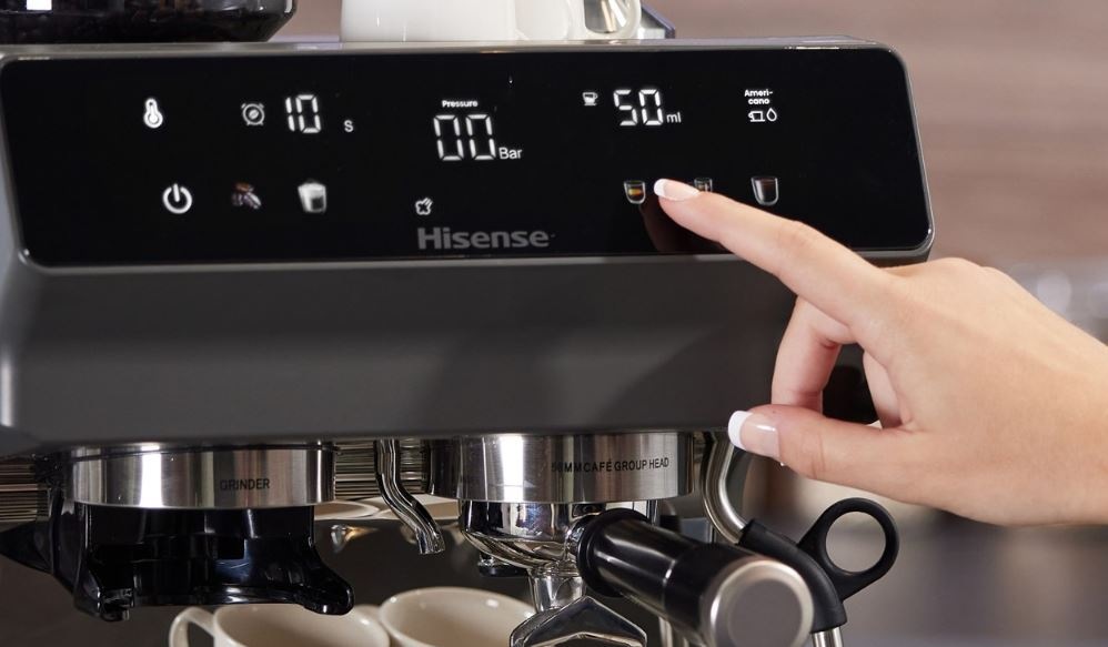 Espresso Hisense HSACM20LP antracitový ženská ruka ovládá kávovar Hisense HSACM20LP pomocí jednoho prstu. Detail na ovládací panel