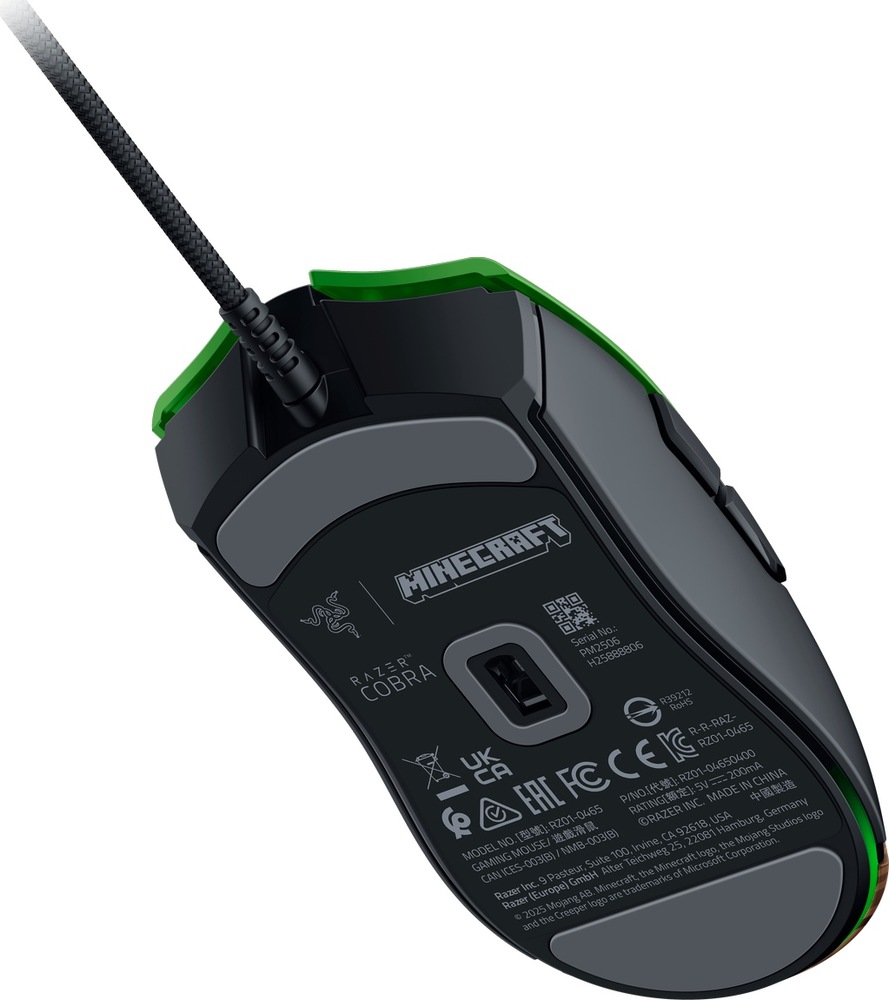 Myš Razer COBRA Lightweight Wired Minecraft Ed. zelená Na obrázku je spodní strana drátové herní myši Razer Cobra Minecraft Edition. Myš má černo-zelené provedení, opletený kabel a na spodní části je vidět optický senzor uprostřed. Kolem senzoru jsou šedé kluzné plošky pro hladký pohyb po podložce. Na těle jsou také loga Razer Cobra, Minecraft a technické údaje produktu. Na boku jsou částečně vidět boční tlačítka.