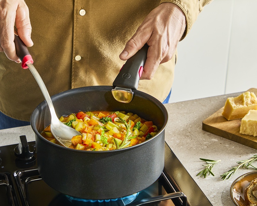 Rendlík Tefal Ingenio Excellence+ P0073053, 20 cm černý Muž jednou rukou nabírá naběračkou zeleninu a druhou drží rukojeť.