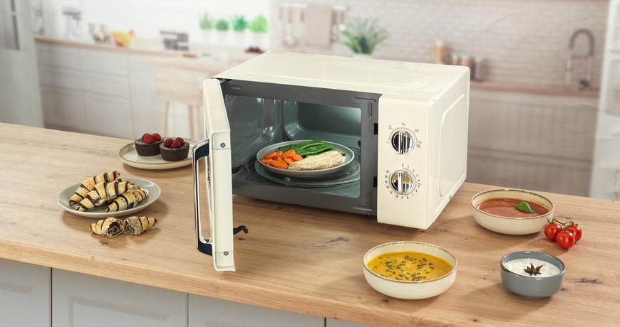Mikrovlnná trouba Gorenje Retro MO20E1HRL béžová Retro mikrovlnka Gorenje MO20E1HRL je položená na kuchyňské lince. Dvířka má pootevřená a kolem ní jsou naskládané potraviny.