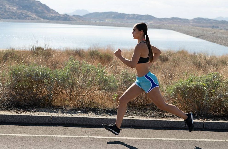 Sluchátka JBL Endurance Run3 BT bílá Žena běžící podél vody s nasazenými sluchátky.