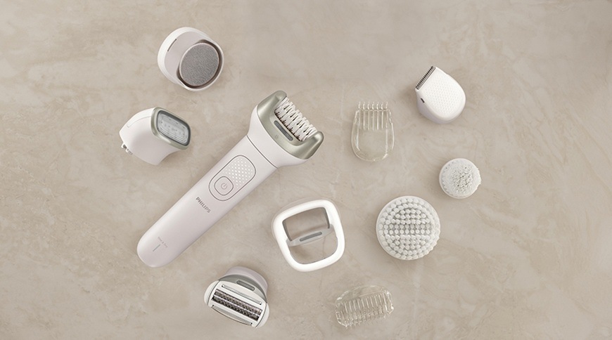 Epilátor Philips BRE750/00 v bílé barvě s rozloženým příslušenstvím, kolem přístroje jsou různé nástavce včetně holicí hlavice, exfoliačního kartáče, nástavce na citlivé oblasti a dalšího příslušenství pro péči o pokožku.