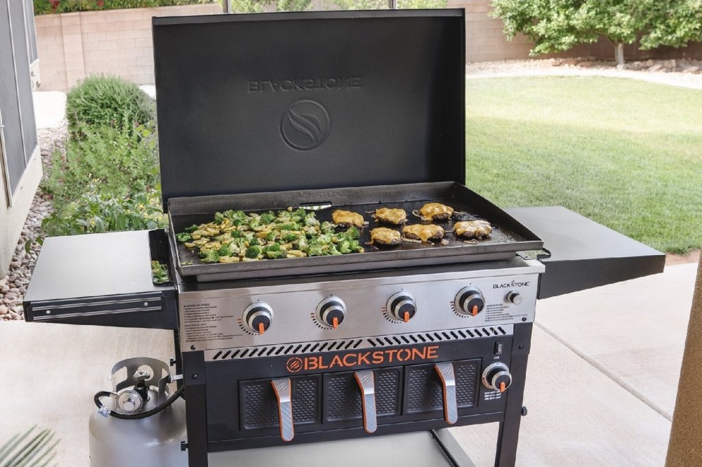Grilování zeleniny a hamburgerů na rozehřáté desce grilu Blackstone 36" v zahradě.