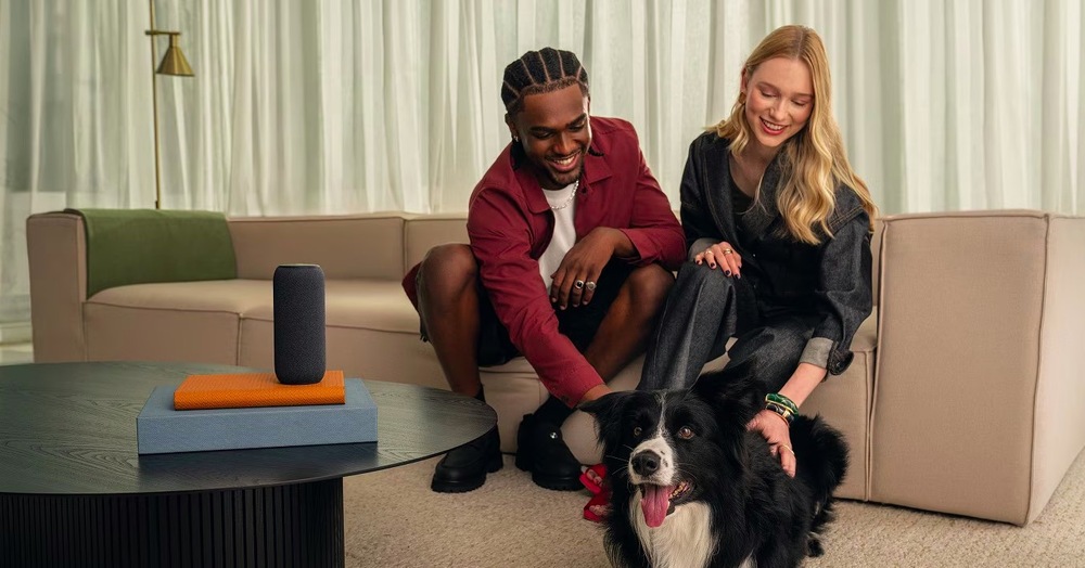 Muž s ženou sedí na pohovce, hladí psa a na stole mají reproduktor Motorola Moto Sound Flow