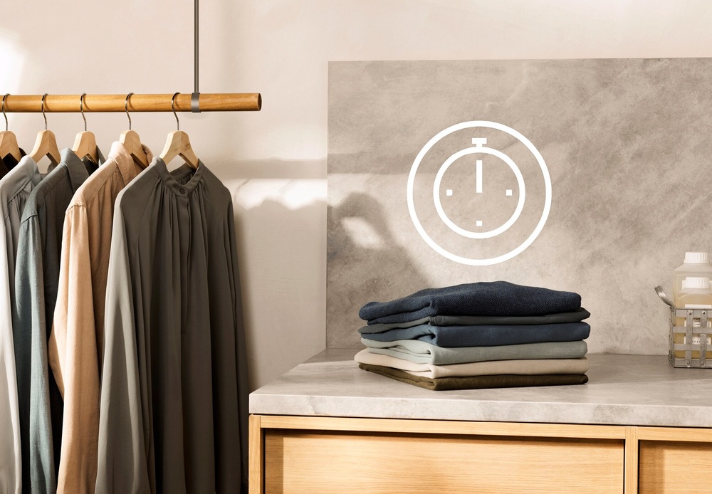 Pračka Electrolux SensiCare 600 EW6T836C bílá Symbol úspory času nad hromádkou poskládaného prádla. Vlevo košile pověšené na ramínku.