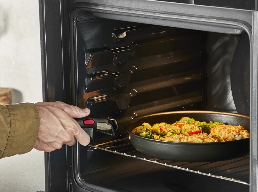 Muž vkládá do vestavné trouby pánev značky Tefal.