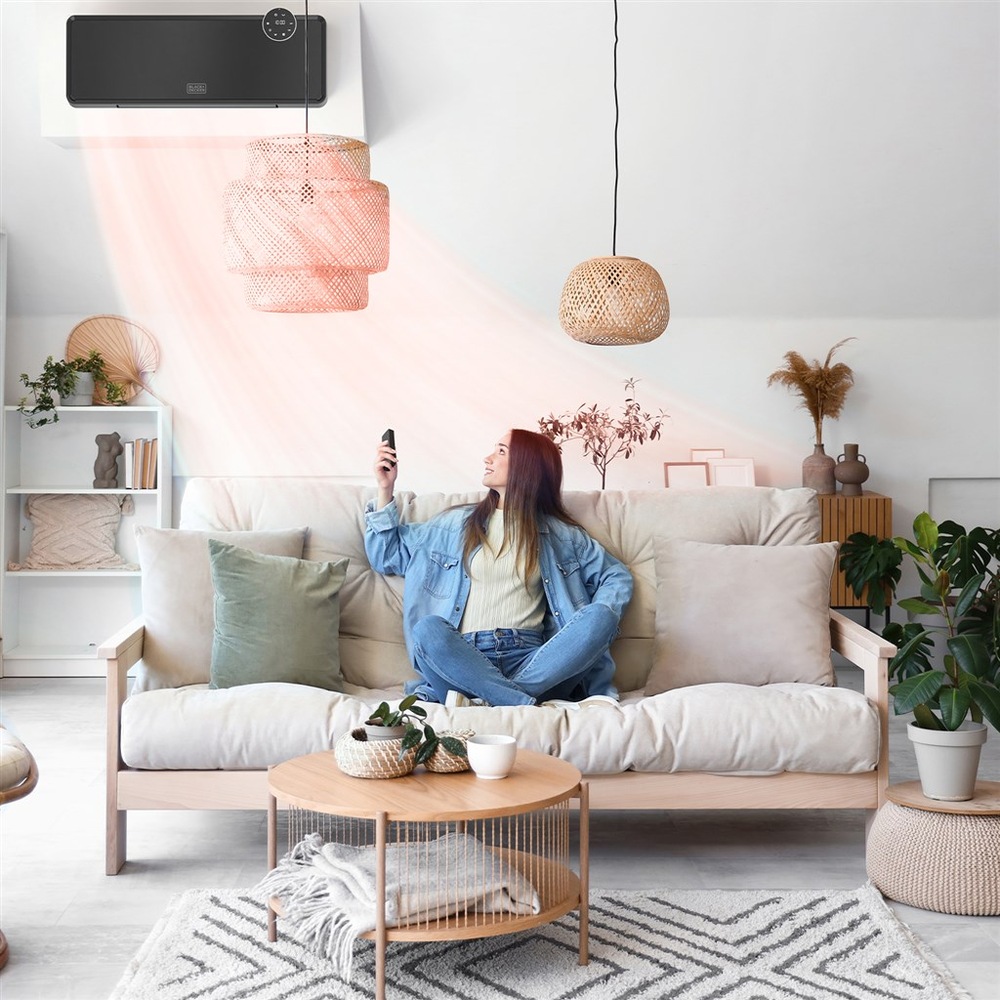 Topný panel Black+Decker BXWSH2001E černý Žena sedí na gauči, v ruce ovladačem míří na topný panel Black+Decker