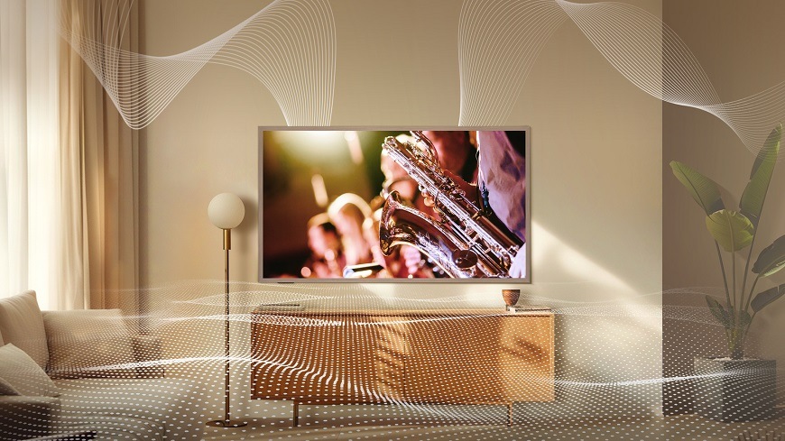 Televize Hisense v obývacím pokoji. Visi na zdi vedle lampy a promíta se na ní koncert, detail hudebniho nastroje. Kolem TV jsou zvukove vlny.