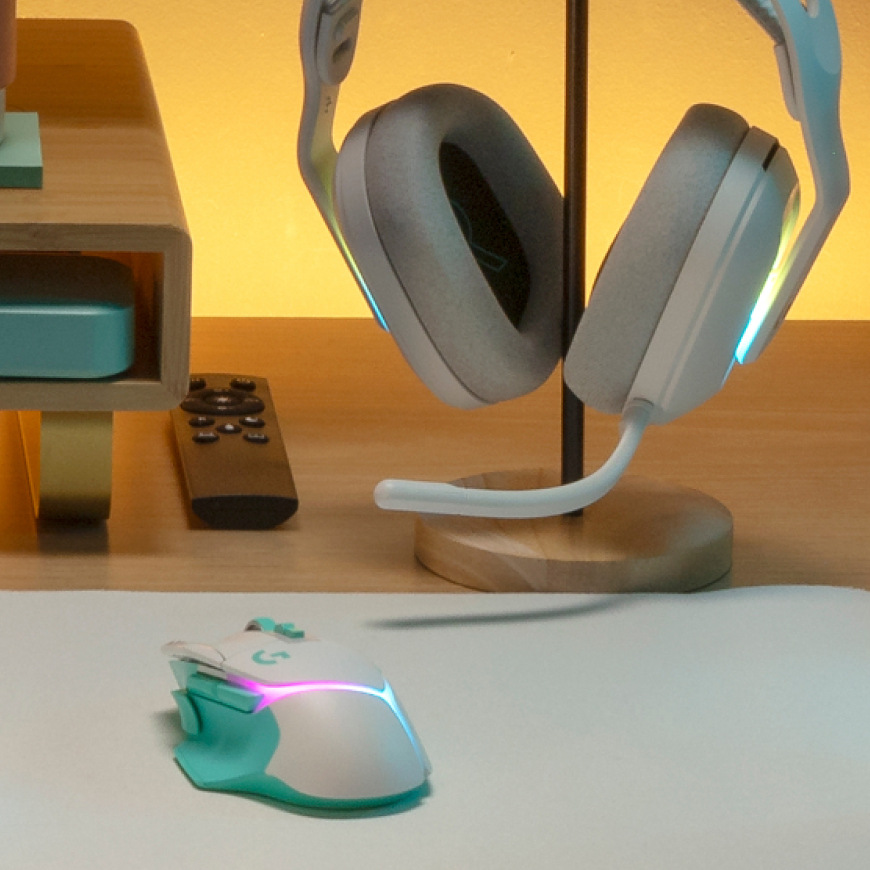 Myš Logitech G502 X Plus položená na stole vedle herního headsetu na stojanu