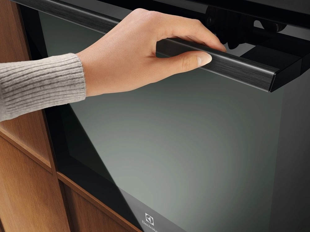 Žena drží madlo trouby Electrolux a zavírá dvířka.