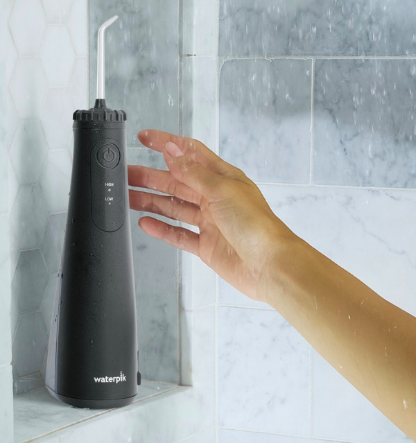 Ruka sahá po voděodolné ústní sprše Waterpik WF26EUB umístěné ve sprše