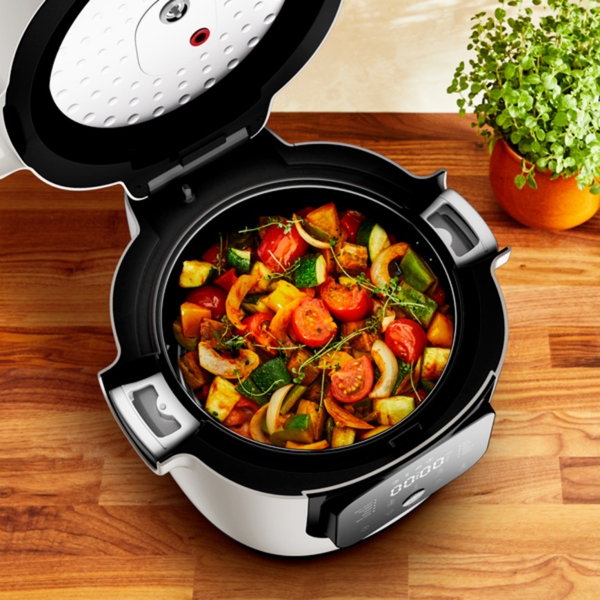 Otevřený multifunkční hrnec Tefal MY700BF0 Multicook připravuje barevnou směs pečené zeleniny s rajčaty cuketou a paprikou na dřevěné kuchyňské lince.