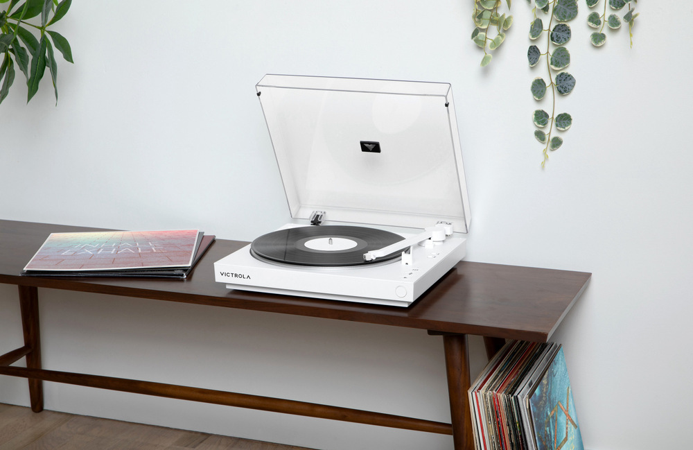 Gramofon Victrola VPT-800 Automatic bílý Victrola VPT-800 Automatic při poslechu vinylu v obývacím pokoji, otevřený kryt a desky uložené pod stolkem