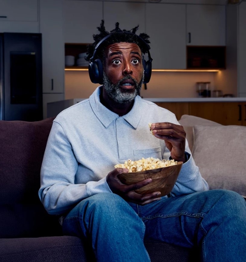 Sluchátka Sennheiser RS275 TV černá Muž s mísou popcornu je ponořený do sledování filmu se sluchátky Sennheiser RS275 TV