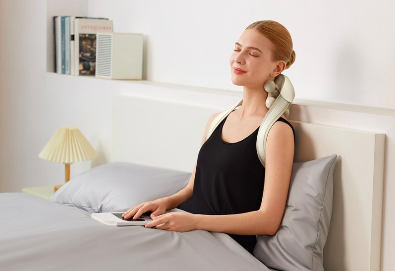 Žena relaxuje s masážním límcem SKG H7 Ultra při odpočinku v posteli