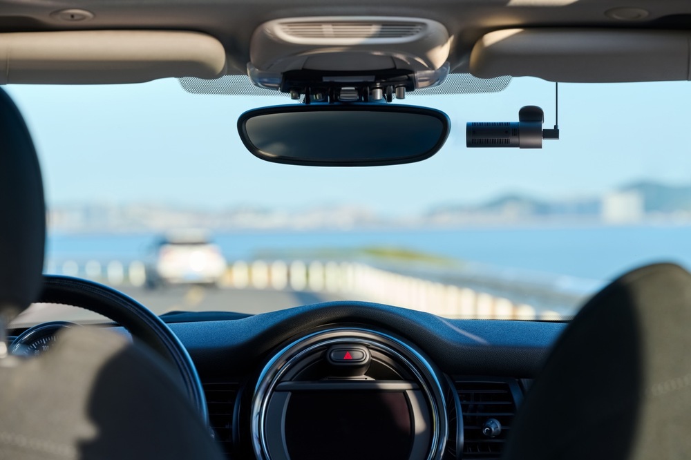 Pohled z interiéru automobilu na autokameru 70mai M310 Plus 4K připevněnou v horní části čelního skla vedle zpětného zrcátka.