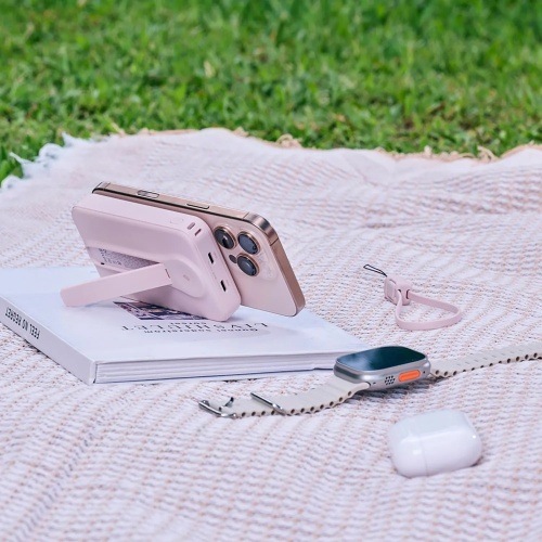 Powerbanka ADAM Elements VIONTA C2 Pro 8-in-1 10000 mAh růžová Piknik na trávníku: powerbanka Adam Elements v růžové drží iPhone na stojánku vedle Apple Watch a AirPods.