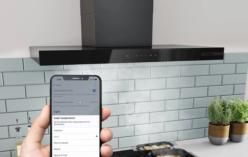 Náhled na mobilní telefon s aplikaci Home Connect, v pozadí varná deska a odsavač par