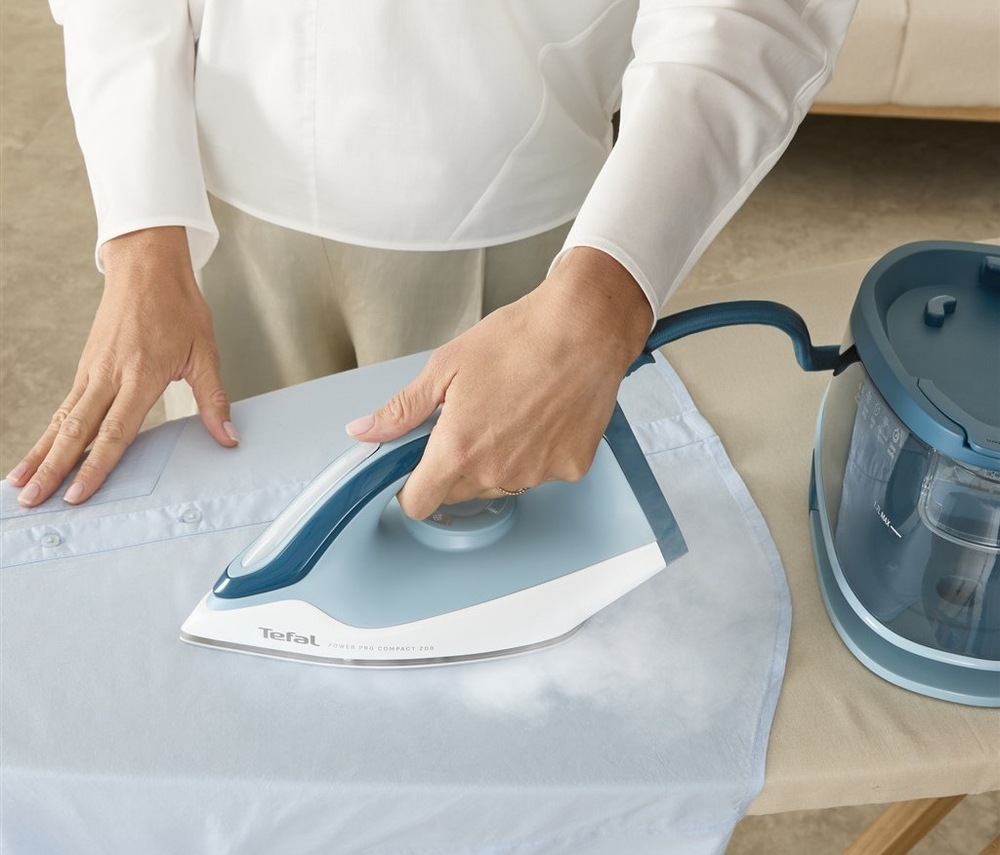 Žehlicí systém Tefal SV6212E0 Power Pro Compact 200 bílý/modrý žena používá parní generátor Tefal SV6212E0 Power Pro Compact 200 pro vyžehlení košile.
