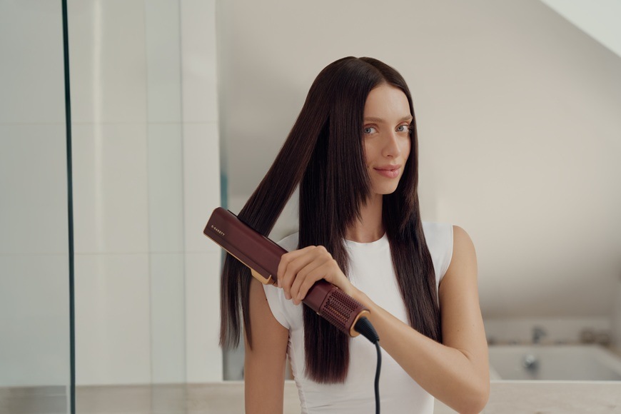 Žehlička na vlasy Garett Beauty AeroGlow hnědá Žena žehlí pramen vlasů.