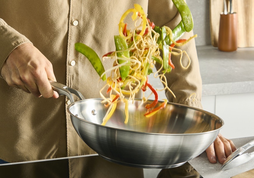 Pánev WOK Tefal Extreme E5291904, 28 cm nerez Muž ve WOK pánvi promíchává kousky zeleniny.