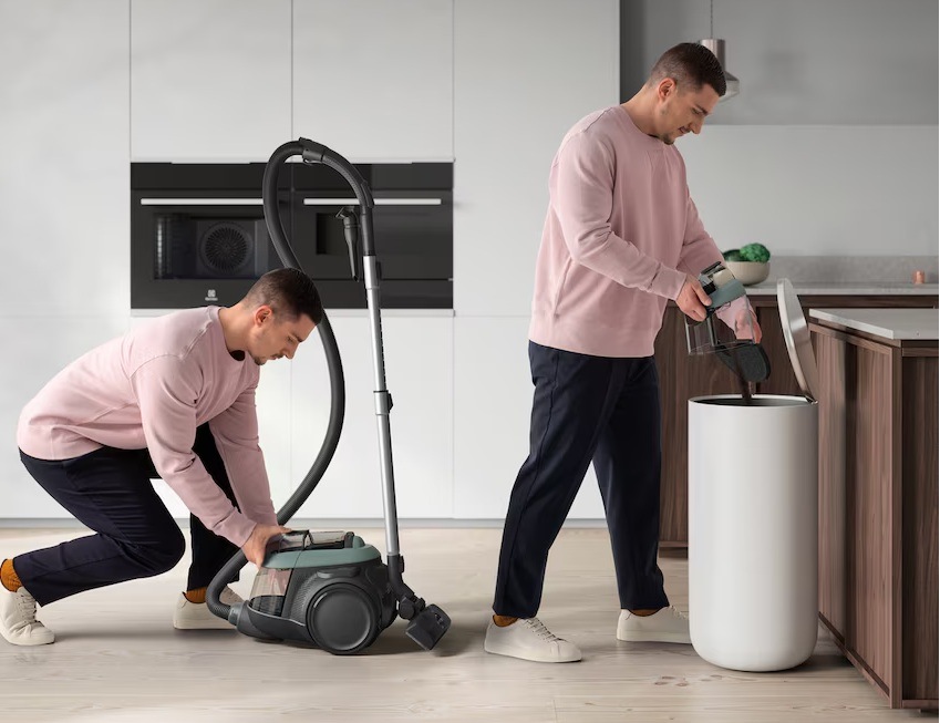 Muž vyndává prachovou nádobu z vysavače Electrolux a v dalším kroku vysypává její obsah do koše. V pozadí je kuchyně s vestavnými spotřebiči Electrolux.