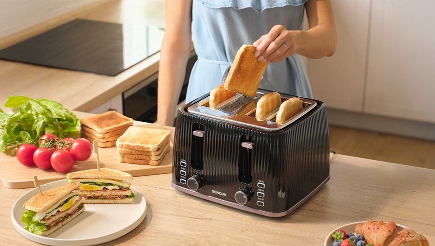 Topinkovač Sencor STS 7541BK černý Žena připravuje snídani a vytahuje toast z topinkovače Sencor v moderní světlé kuchyni.